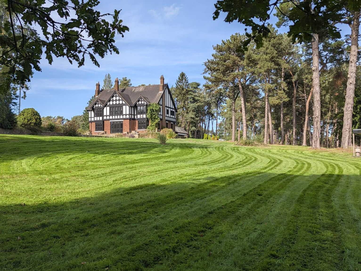 A very large striped lawn framed by trees, with a house in the distance.