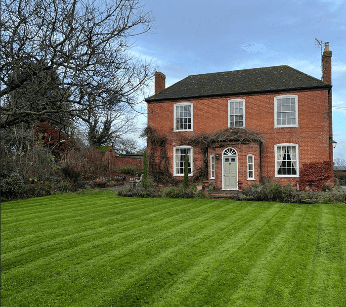 A red-brick house behind a freshly striped lawn.